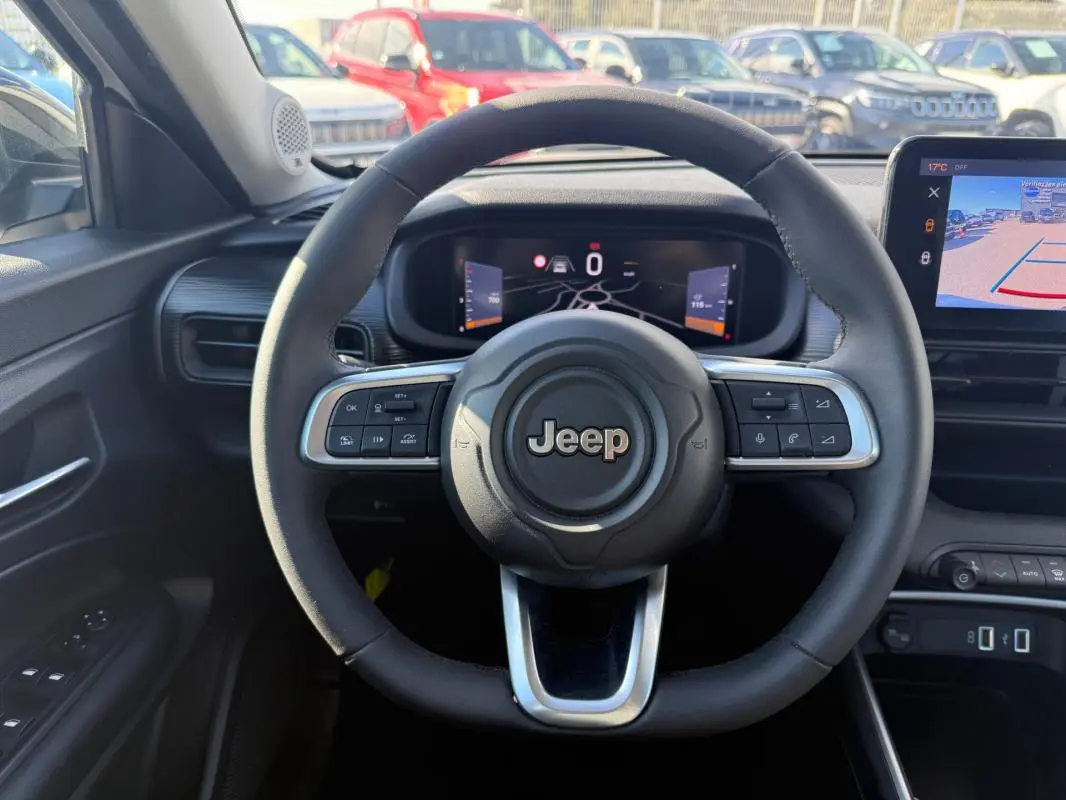 Vue intérieure centrée sur le volant Jeep noir avec tableau de bord numérique et écran de caméra de recul.