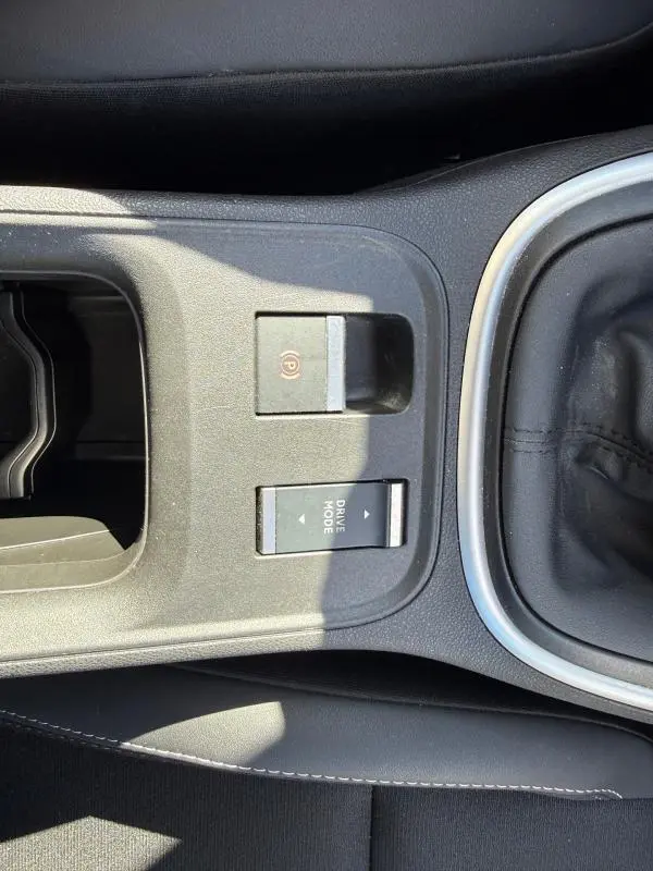 Vue rapprochée de la console centrale noire du Jeep Avenger 2025 avec frein à main électrique et bouton Drive Mode.