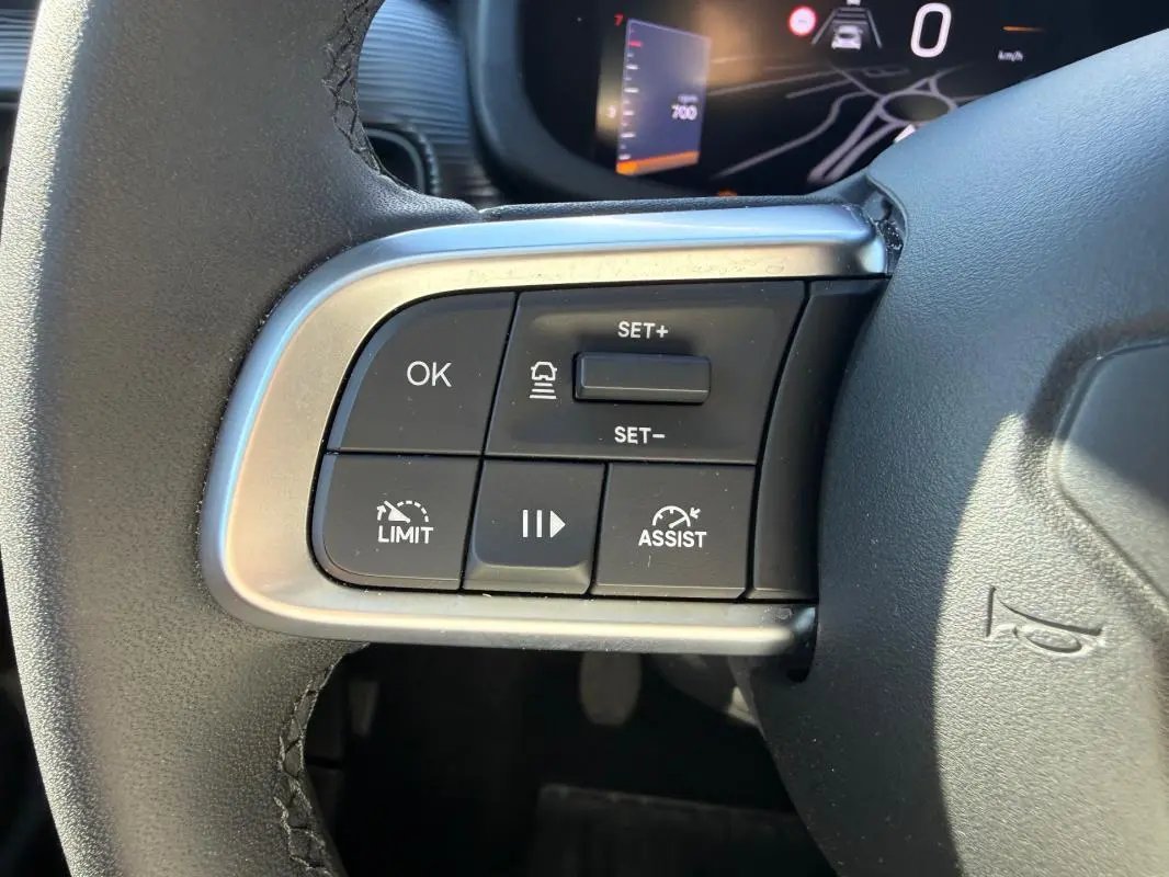 Gros plan sur les commandes du volant côté gauche du Jeep Avenger blanc, avec régulateur de vitesse et assistant de conduite.