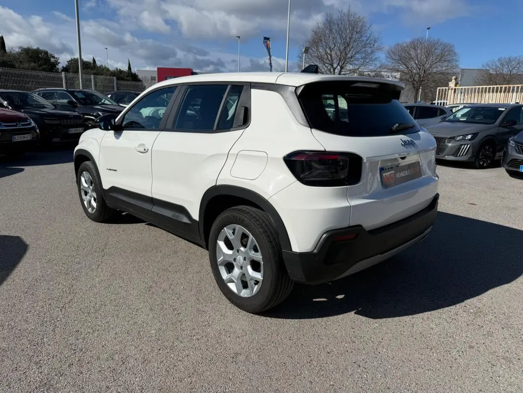 Jeep Avenger blanc en vue 3/4 arrière droit, avec jantes alliage 17 pouces et feux arrière noirs teintés.