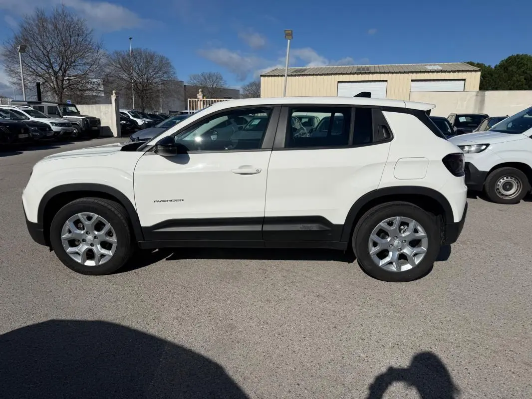 Profil côté gauche d'un Jeep Avenger blanc 2025 avec jantes alliage 17 pouces et protections noires sur bas de caisse.