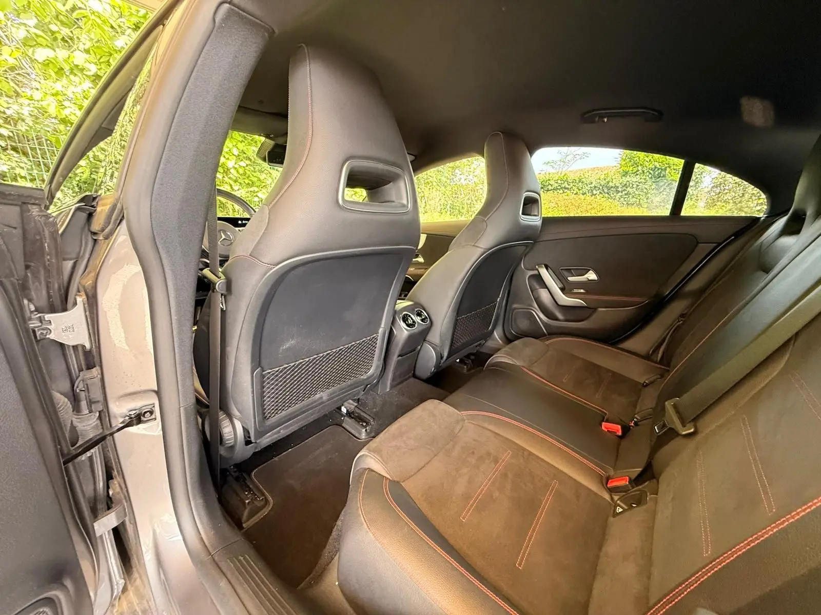 Vue intérieure arrière gauche de la Mercedes Classe CLA 180 D AMG Line gris montagne, sièges sport en cuir noir avec surpiqûres rouges.