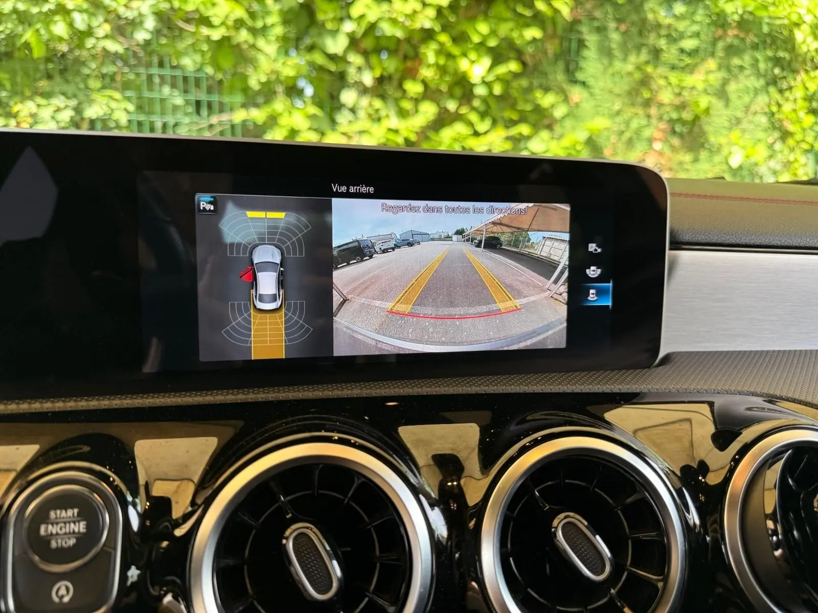 Écran central montrant la caméra de recul et les capteurs de stationnement du tableau de bord d'une Mercedes CLA gris montagne.