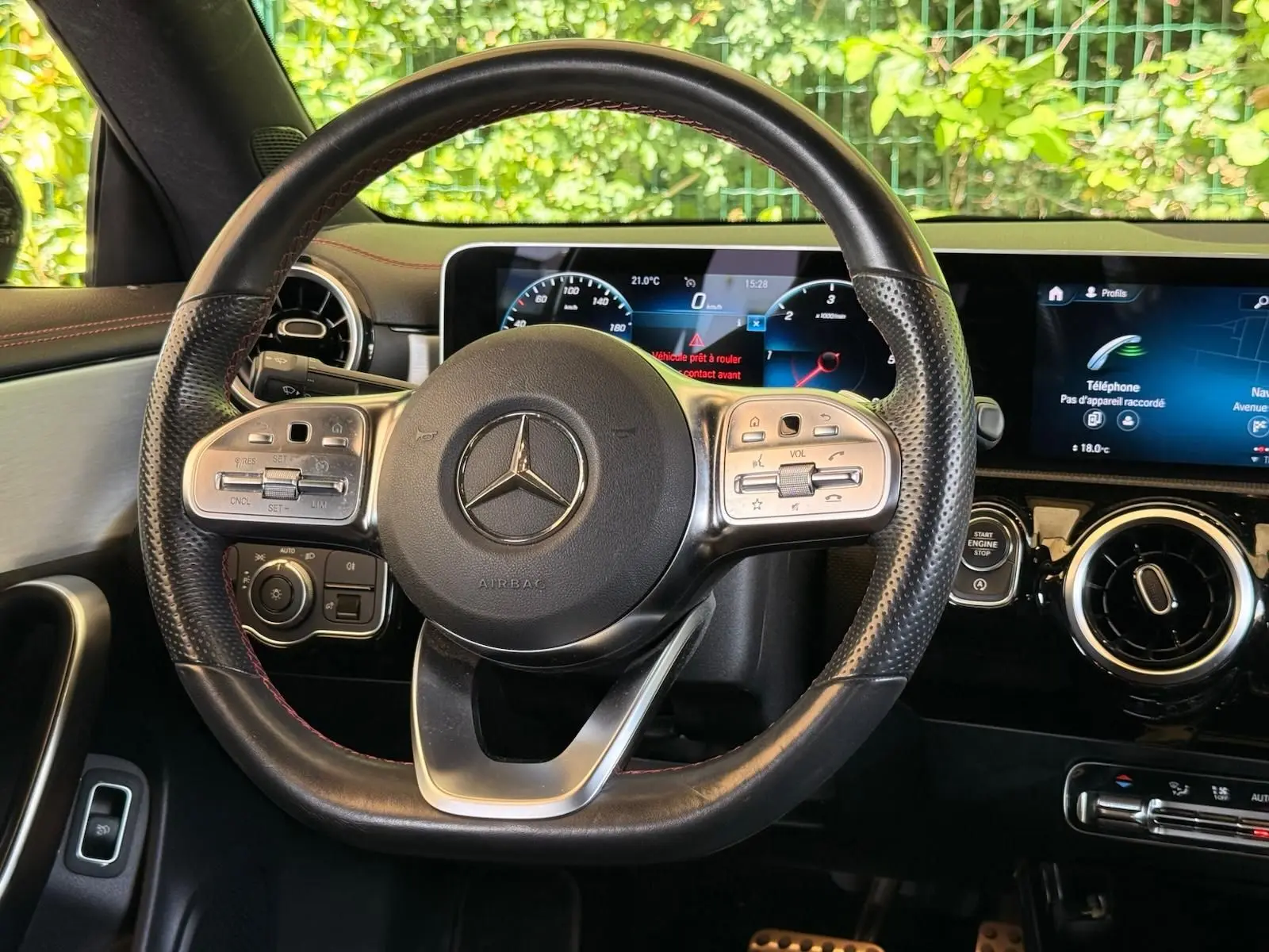 Vue intérieure centrée sur le volant cuir perforé et les écrans numériques du tableau de bord d'une Mercedes CLA gris montagne.