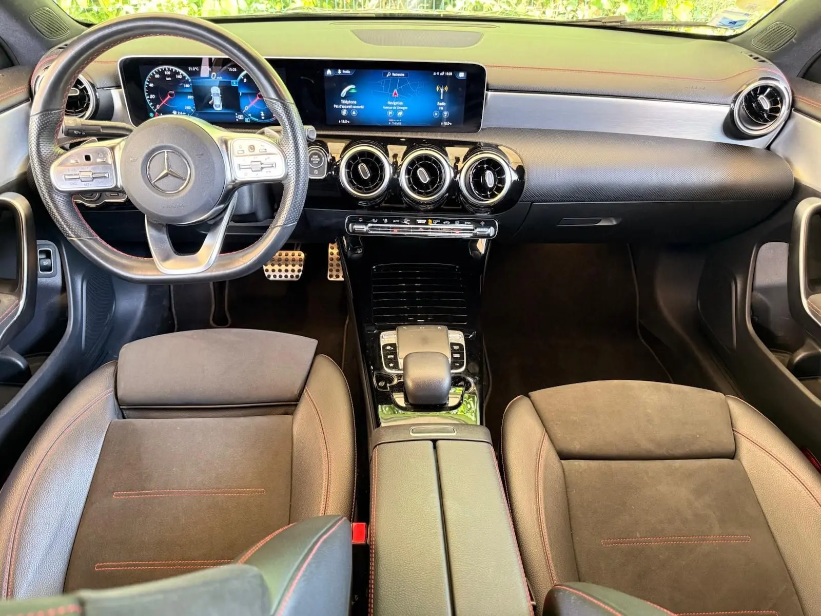 Vue intérieure avant de la Mercedes Classe CLA 180 D AMG Line 2019, tableau de bord moderne avec écran large et sièges en cuir noir à surpiqûres rouges.