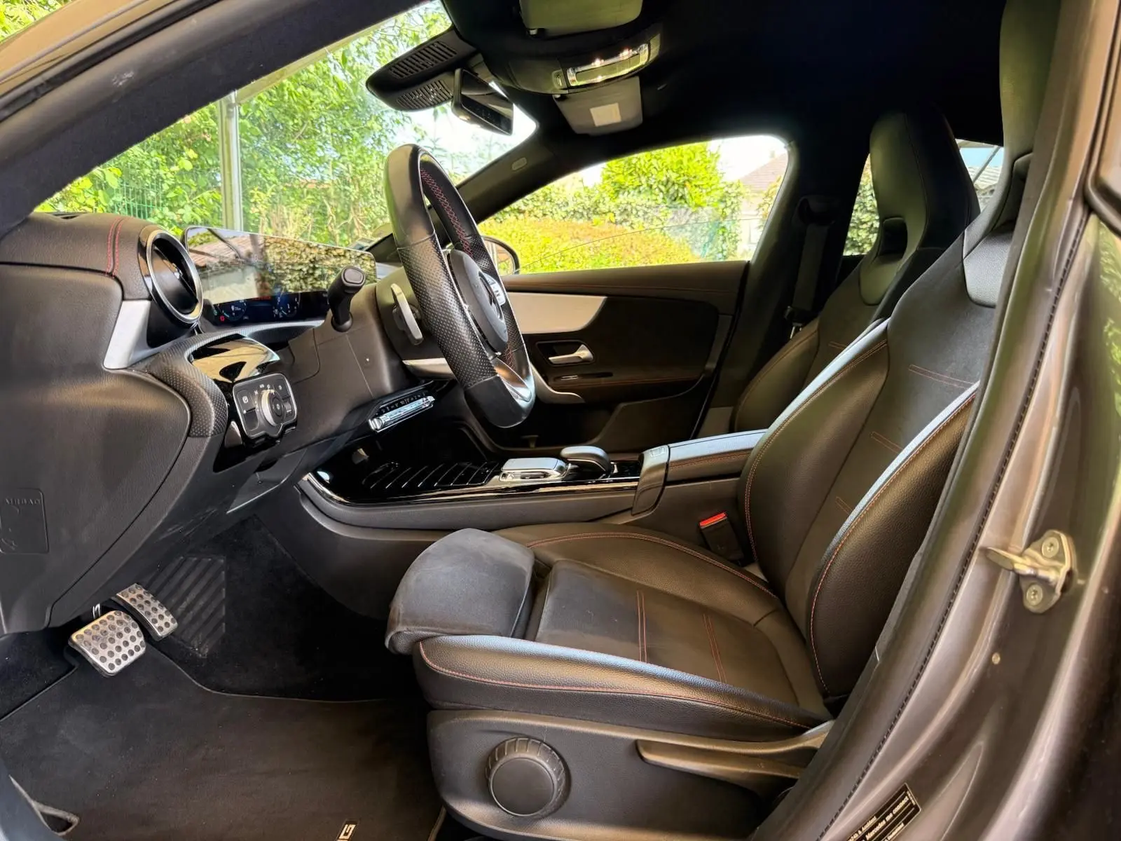 Vue intérieure côté conducteur de la Mercedes Classe CLA 180 D AMG Line 2019 avec sièges cuir noir et surpiqûres rouges.