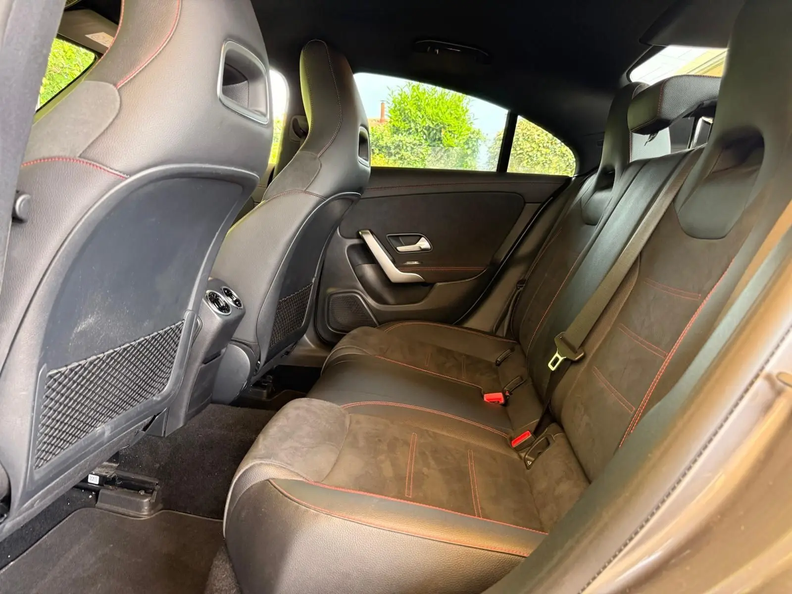 Vue intérieure arrière droite de la Mercedes Classe CLA 180 D AMG Line 2019 avec sièges en cuir noir et surpiqûres rouges.