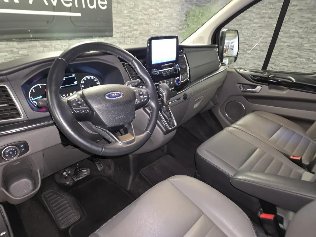 Vue intérieure côté conducteur du Ford Transit Custom noir, montrant le volant cuir, tableau de bord et sièges gris anthracite.