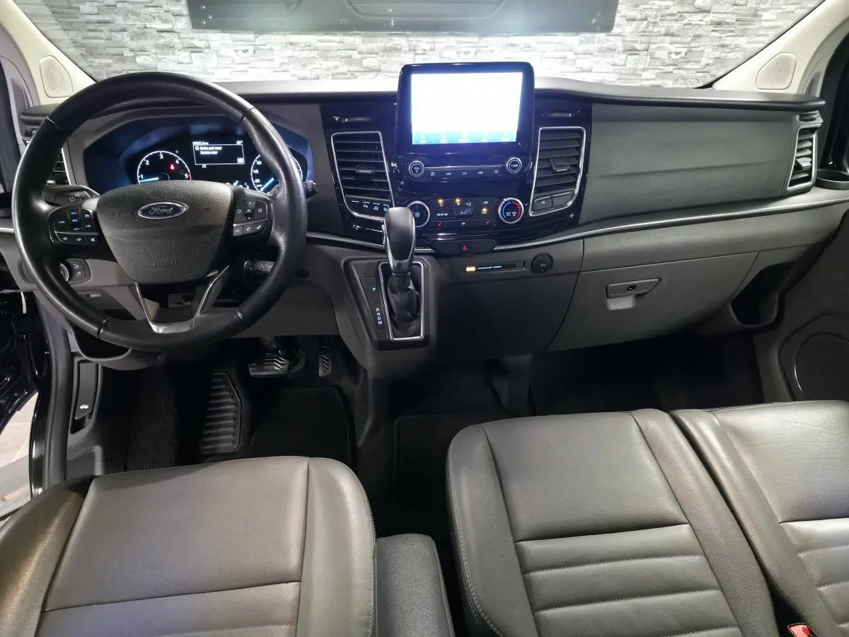 Vue intérieure avant du Ford Transit Custom noir 2022, tableau de bord avec écran tactile et sièges cuir gris anthracite.