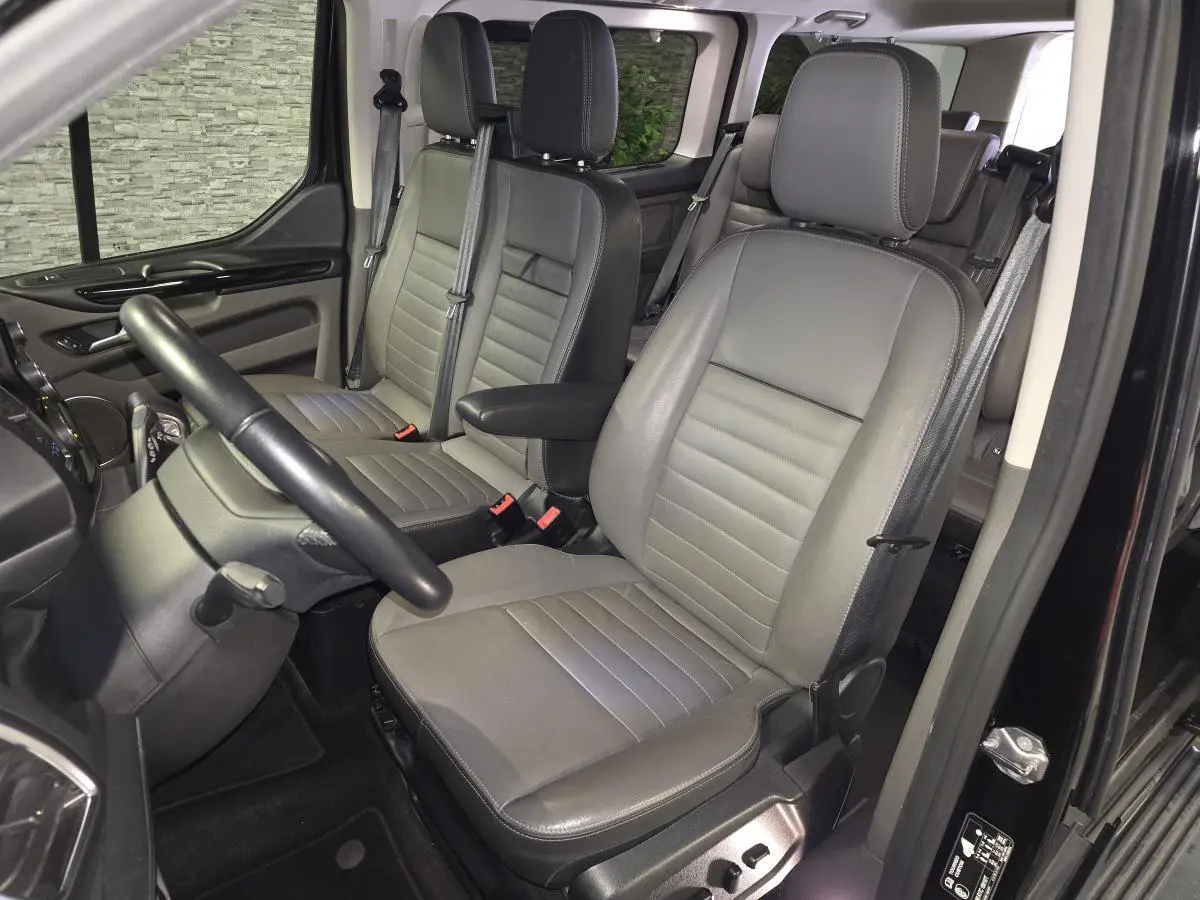 Vue intérieure côté conducteur du Ford Transit Custom noir, sièges en cuir gris anthracite avec accoudoirs et réglages électriques.