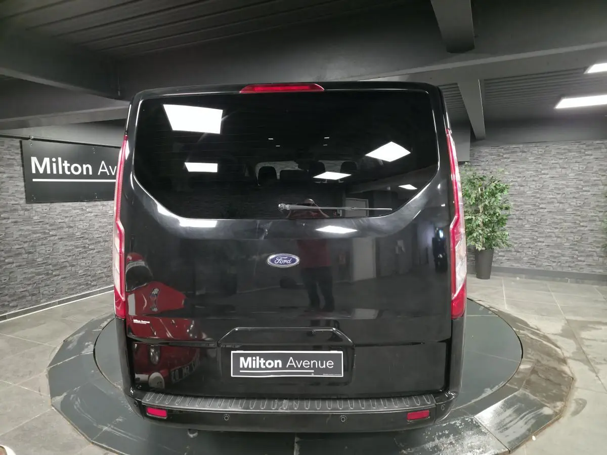 Vue arrière d'un Ford Transit Fourgon Custom noir, avec hayon vitré et feux verticaux intégrés.