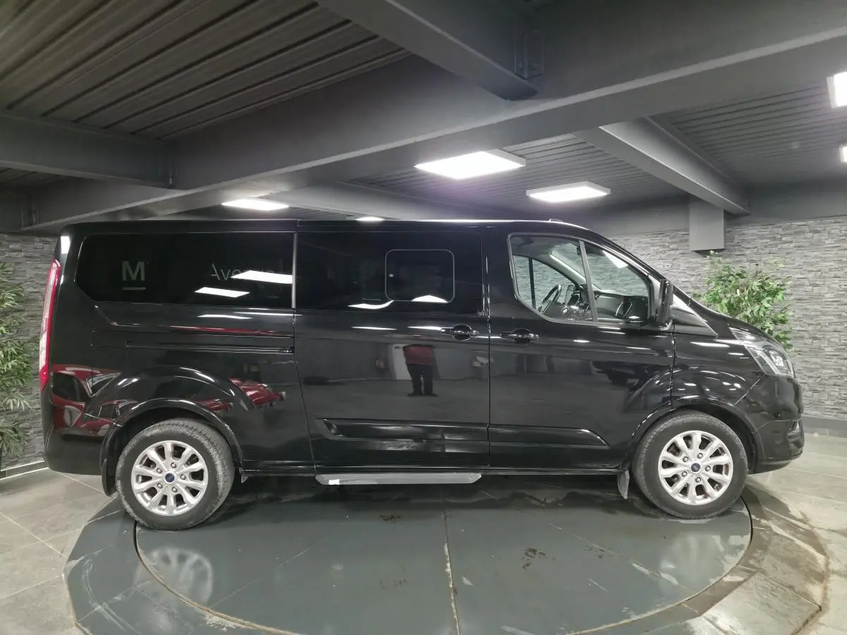 Vue de profil côté gauche d’un Ford Transit Fourgon Custom noir métallisé, avec jantes alliage et portes coulissantes.