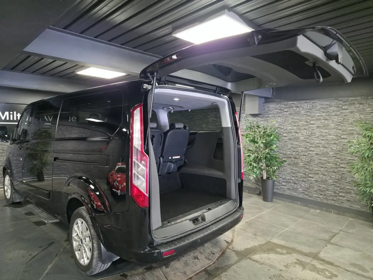 Vue 3/4 arrière droite d’un Ford Transit Fourgon Custom noir avec hayon ouvert montrant l’espace de chargement intérieur.