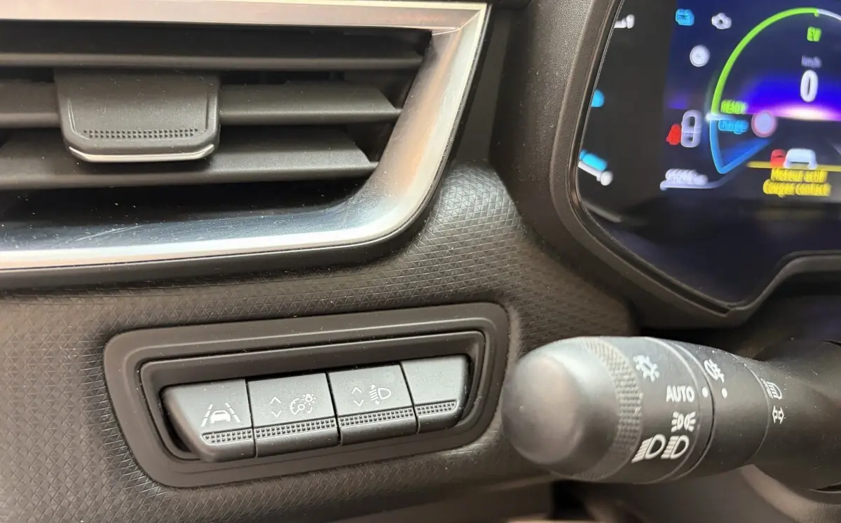 Gros plan sur les commandes d’aide à la conduite et réglage des phares dans l’habitacle d’une Renault Clio blanche hybride 2022.