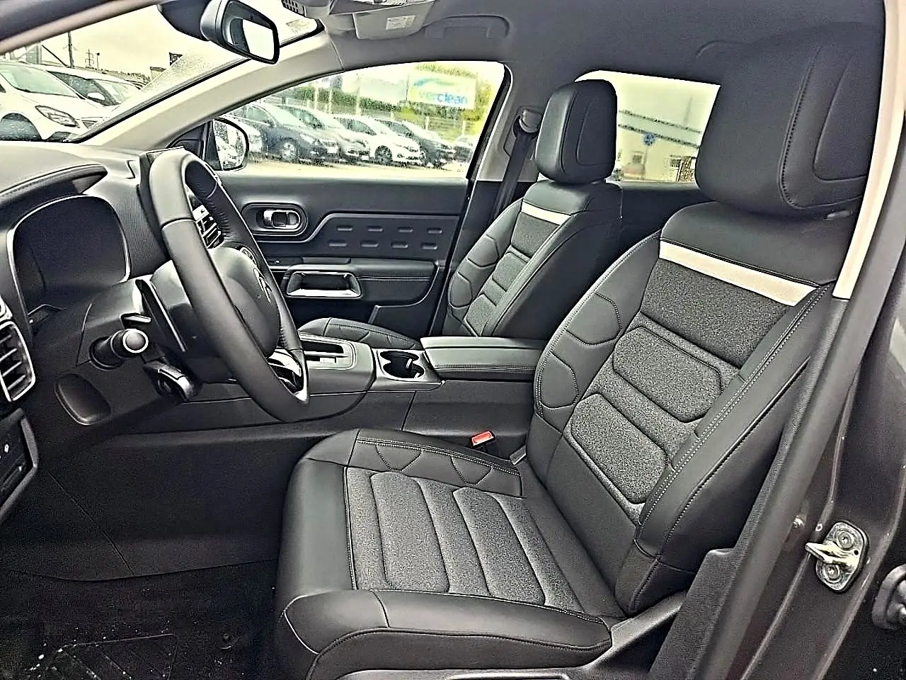 Vue intérieure côté conducteur du Citroën C5 Aircross 2025, sièges noirs cuir et tissu avec accoudoir central.