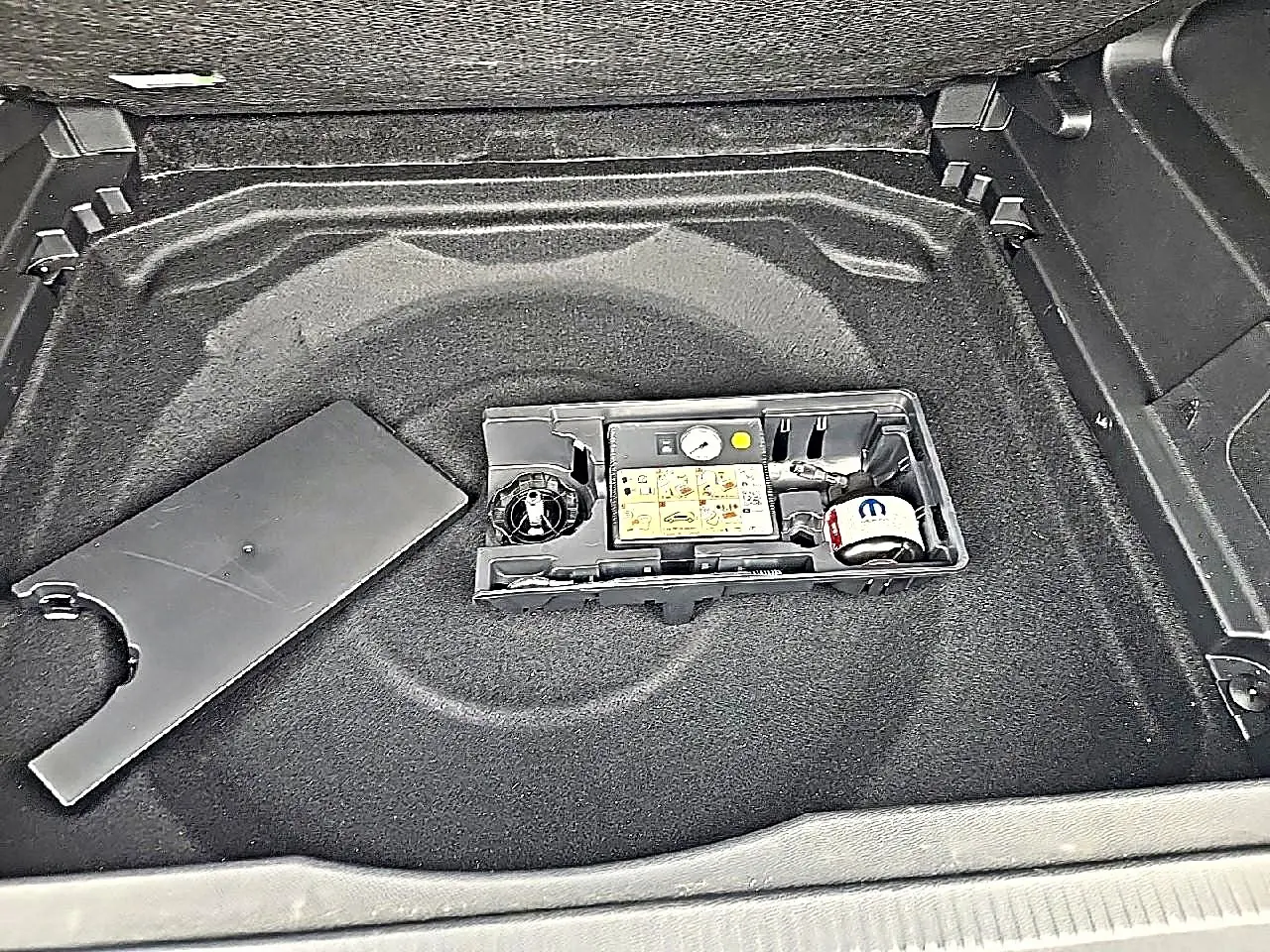 Vue plongeante sur le coffre gris du Citroën C5 Aircross 2025, montrant le rangement sous plancher avec kit de réparation pneus.