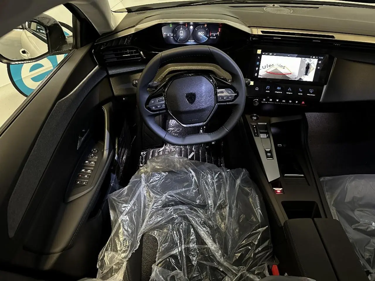 Vue intérieure avant de la Peugeot 308 2024 blanc okenite, volant compact, tableau de bord numérique et écran central tactile allumé.