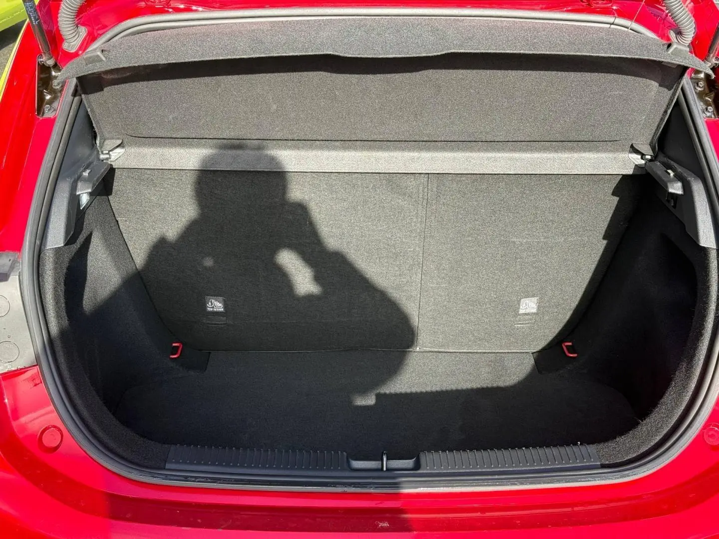 Coffre ouvert vu de face d’une MG3 1.5 Hybrid+ 195ch Luxury en rouge métallisé, intérieur noir et tapis propre.