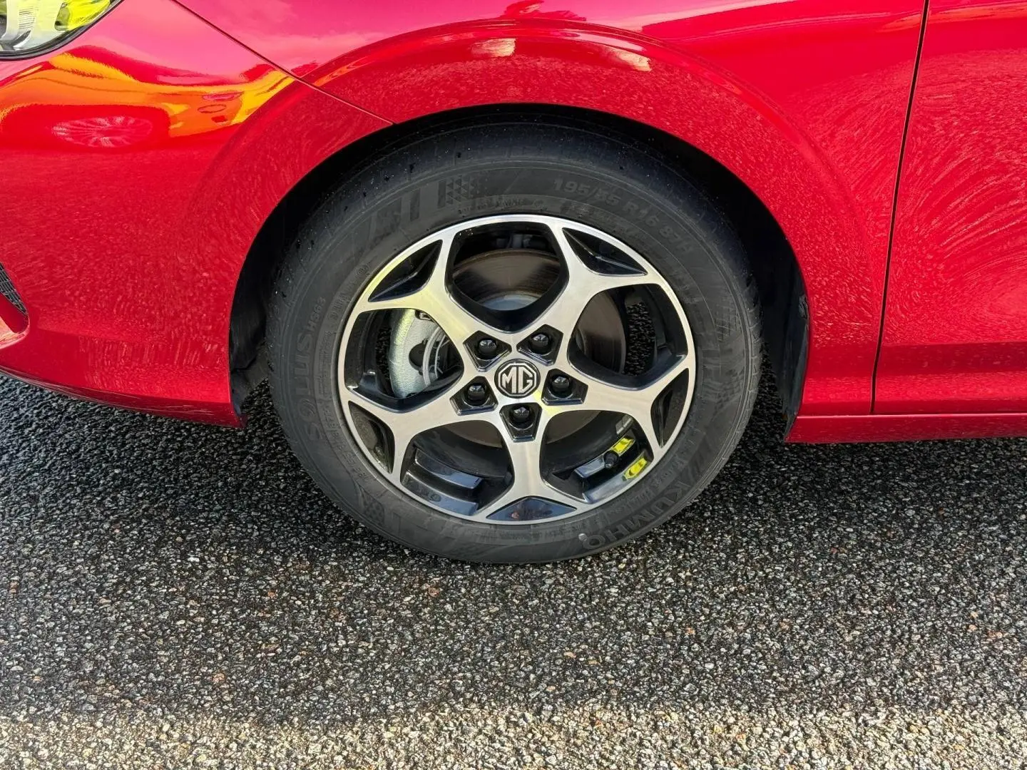 Gros plan sur la roue avant gauche d'une MG3 1.5 Hybrid+ Luxury 2025 en rouge métallisé avec jante alu bicolore.