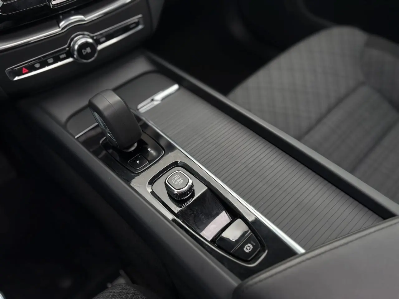 Gros plan sur la console centrale noire du Volvo XC60 2024 avec bouton start/stop et levier de vitesse automatique.