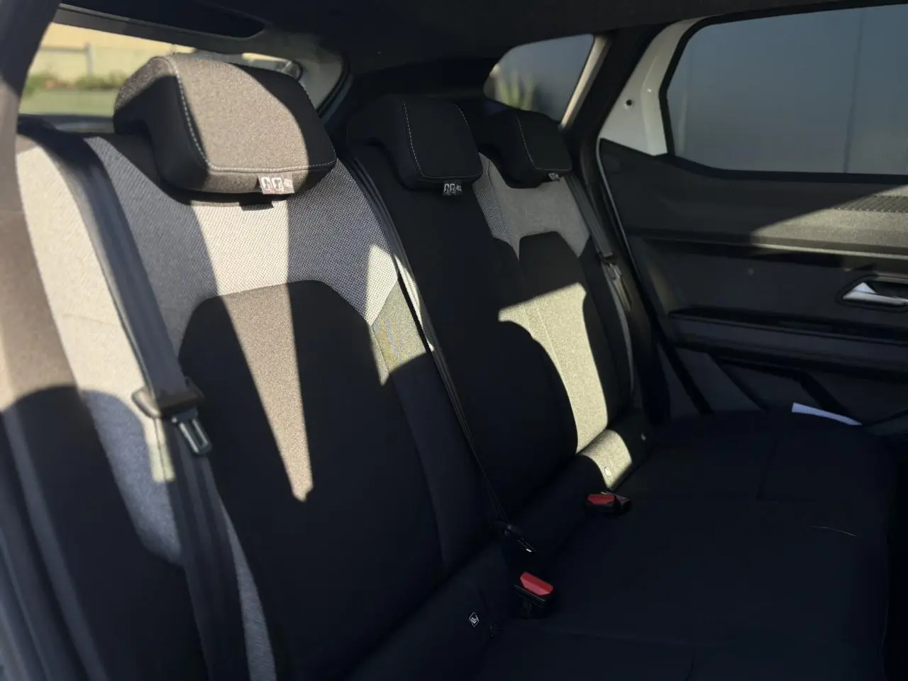 Vue latérale intérieure montrant la banquette arrière noire et grise du Dacia Duster 2025, avec appuie-têtes et ceintures visibles.