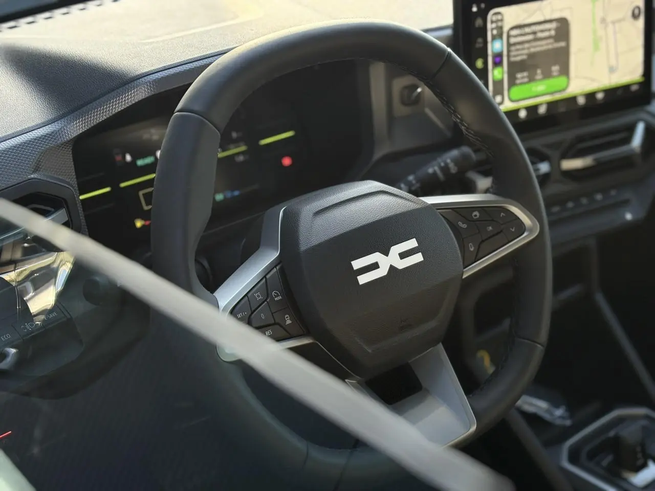 Gros plan sur le volant noir du Dacia Duster 2025 avec commandes intégrées et écran tactile de navigation en arrière-plan.