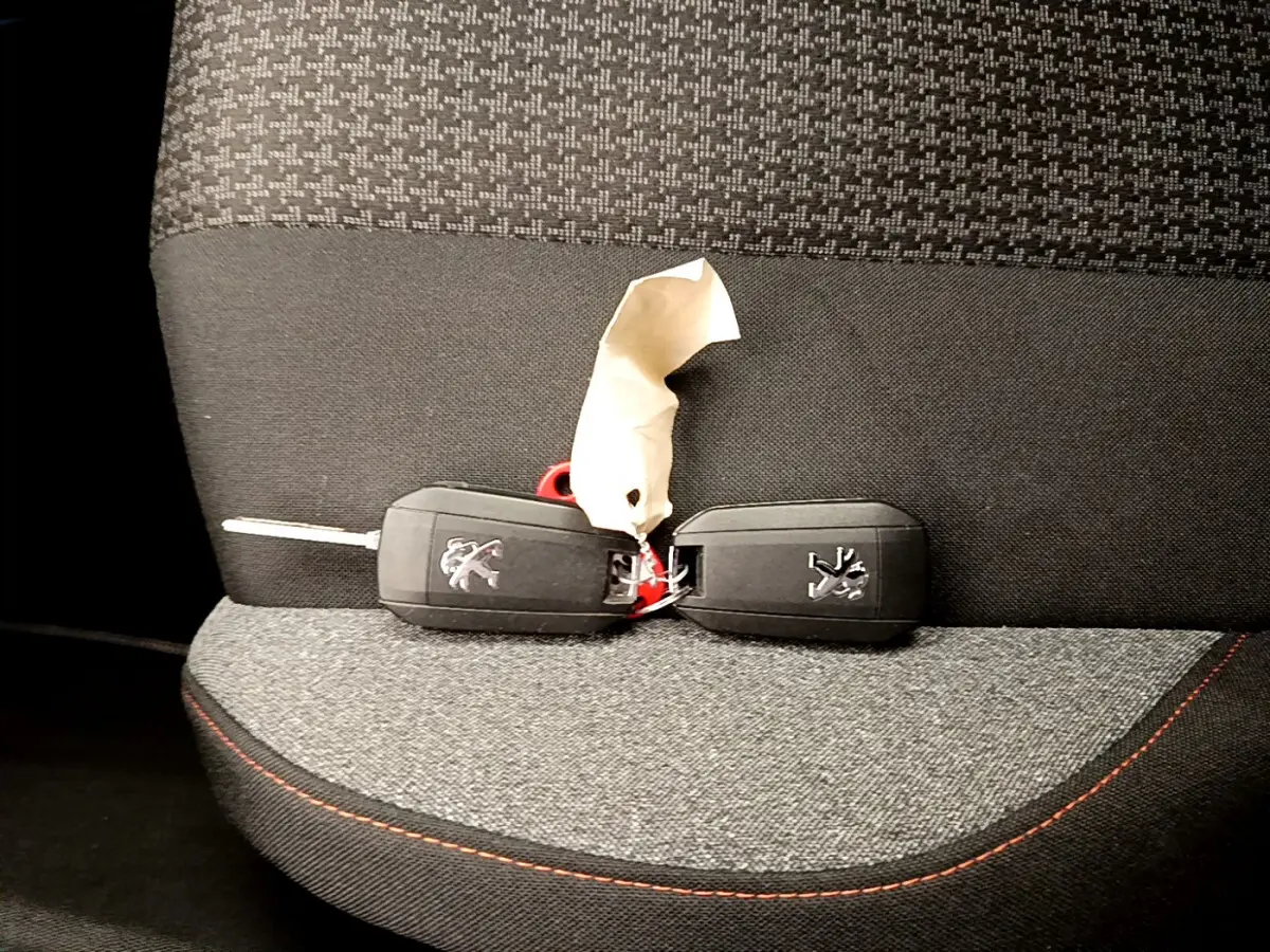Clé de voiture Peugeot posée sur un siège tissu gris foncé avec surpiqûres rouges, intérieur du 3008 Puretech 2020.