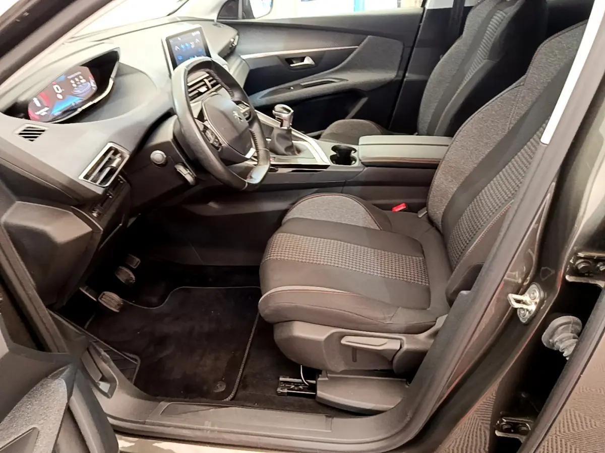 Intérieur côté conducteur du Peugeot 3008 gris foncé 2020, volant cuir, tableau de bord digital et sièges tissu noirs.