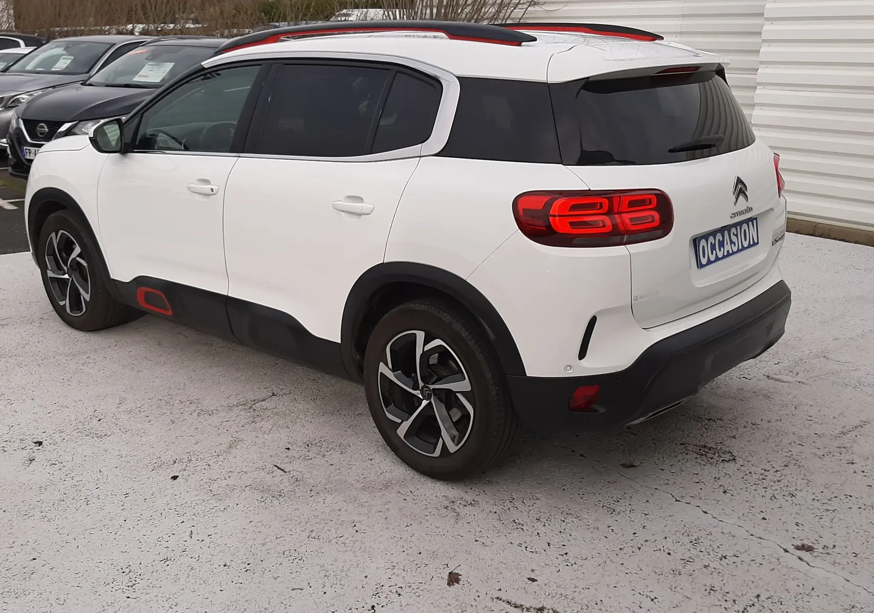 Vue 3/4 arrière droite d'un Citroën C5 Aircross blanc avec toit noir et touches rouges, sur parking extérieur.