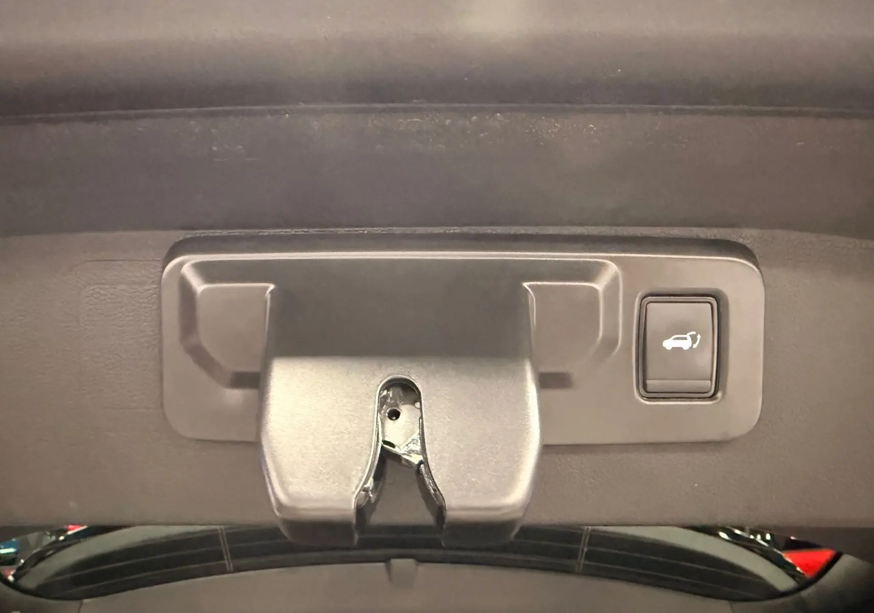 Gros plan sur la poignée intérieure et le bouton d'ouverture du coffre du Renault Austral gris schist avec toit noir.