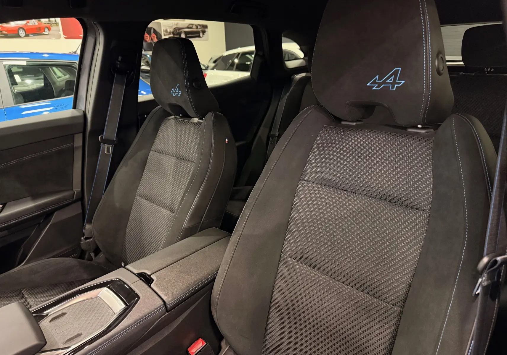 Vue intérieure rapprochée des sièges avant noirs avec surpiqûres bleues et logo Alpine brodé sur les appuie-têtes.