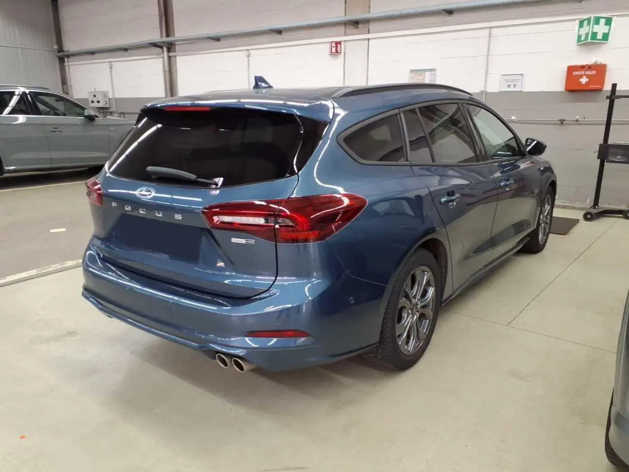 Vue 3/4 arrière droite d'une Ford Focus SW 2023 bleu azur avec attelage et jantes alliage 17 pouces en intérieur d'atelier.