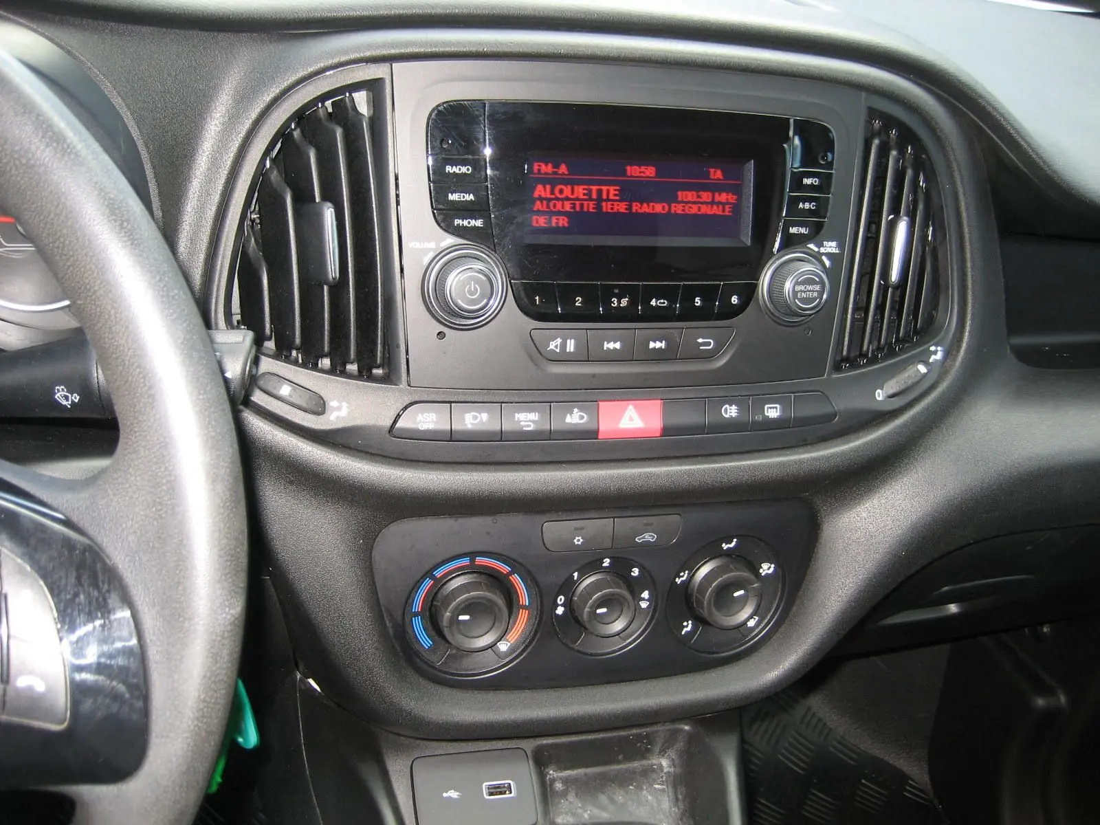 Vue rapprochée du tableau de bord noir du Fiat Doblo Cargo 2018, avec commandes radio et climatisation visibles.