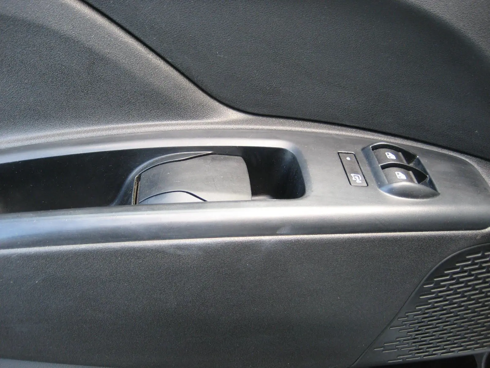 Gros plan sur la commande de lève-vitre et verrouillage sur la porte intérieure côté gauche du Fiat Doblo Cargo blanc.