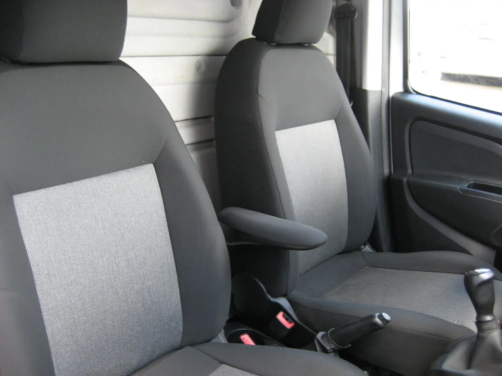 Vue intérieure des sièges avant gris et noir du Fiat Doblo Cargo 2018, avec accoudoir central et levier de vitesses manuel visible.