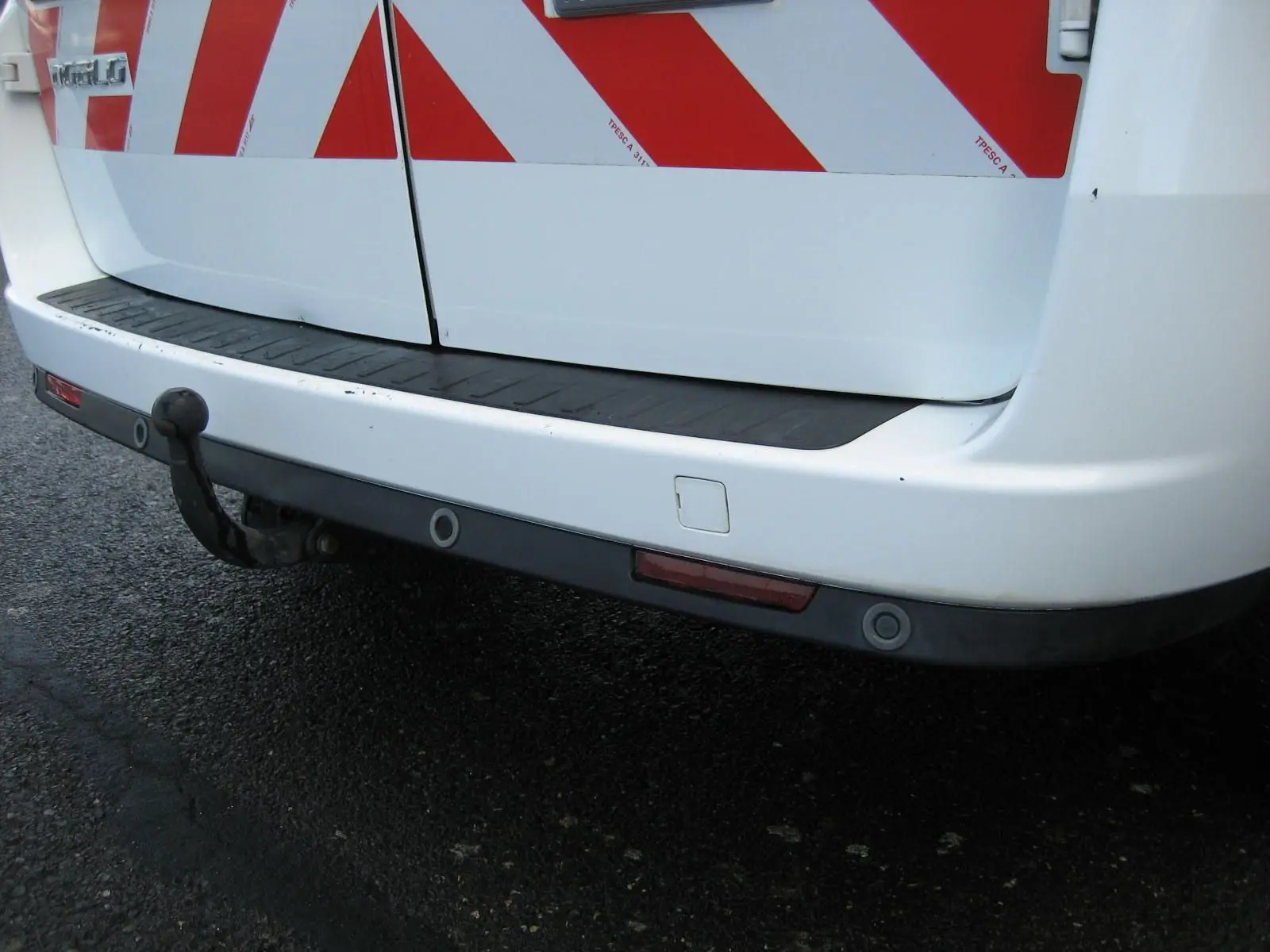 Gros plan sur le pare-chocs arrière blanc du Fiat Doblo Cargo avec attelage et bandes réfléchissantes rouges.