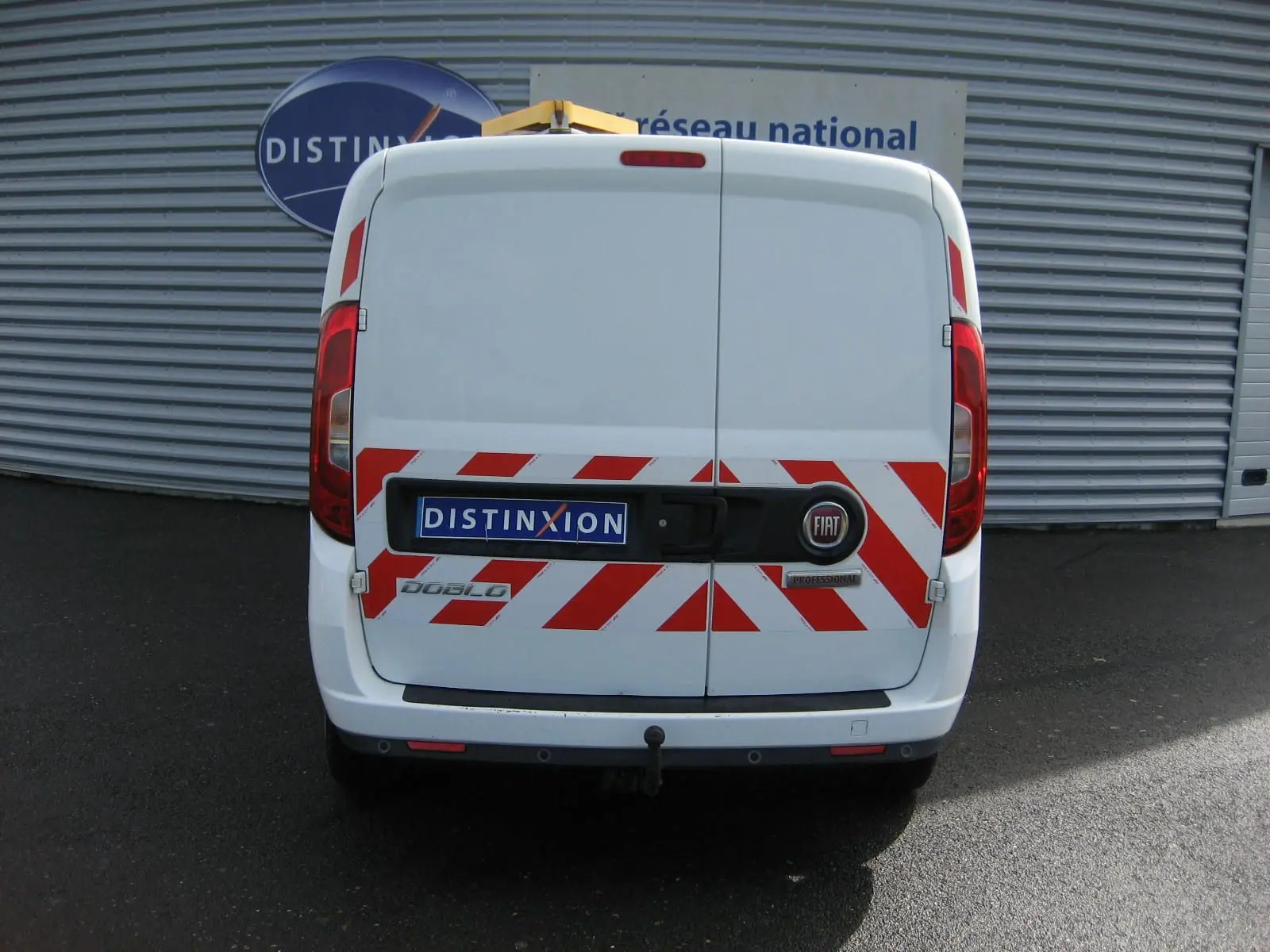 Vue arrière d'un FIAT Doblo Cargo blanc de 2018 avec marquages rouges réfléchissants et attelage visible.
