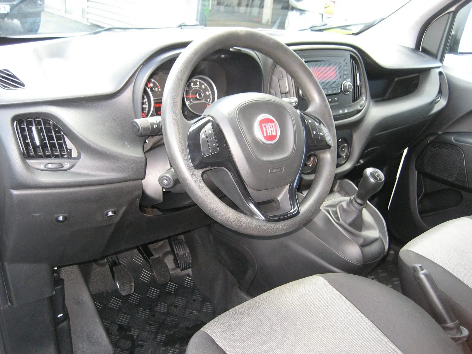 Vue intérieure côté conducteur du Fiat Doblo Cargo 2018, volant multifonction et levier de vitesses manuel visibles.