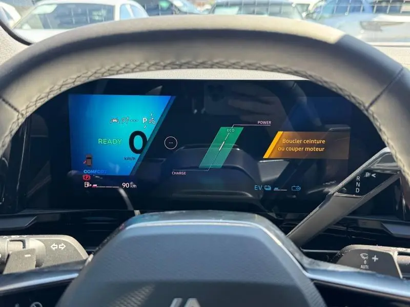 Vue du tableau de bord numérique du Renault Austral 2025 hybride, affichage couleur avec alertes et indicateurs de conduite.