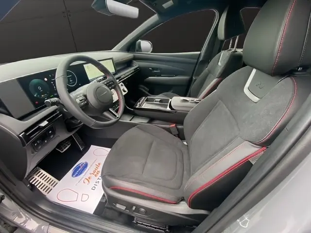 Vue intérieure côté conducteur du Hyundai Tucson 2026 gris foncé, sièges sport noirs avec surpiqûres rouges et tableau de bord numérique.