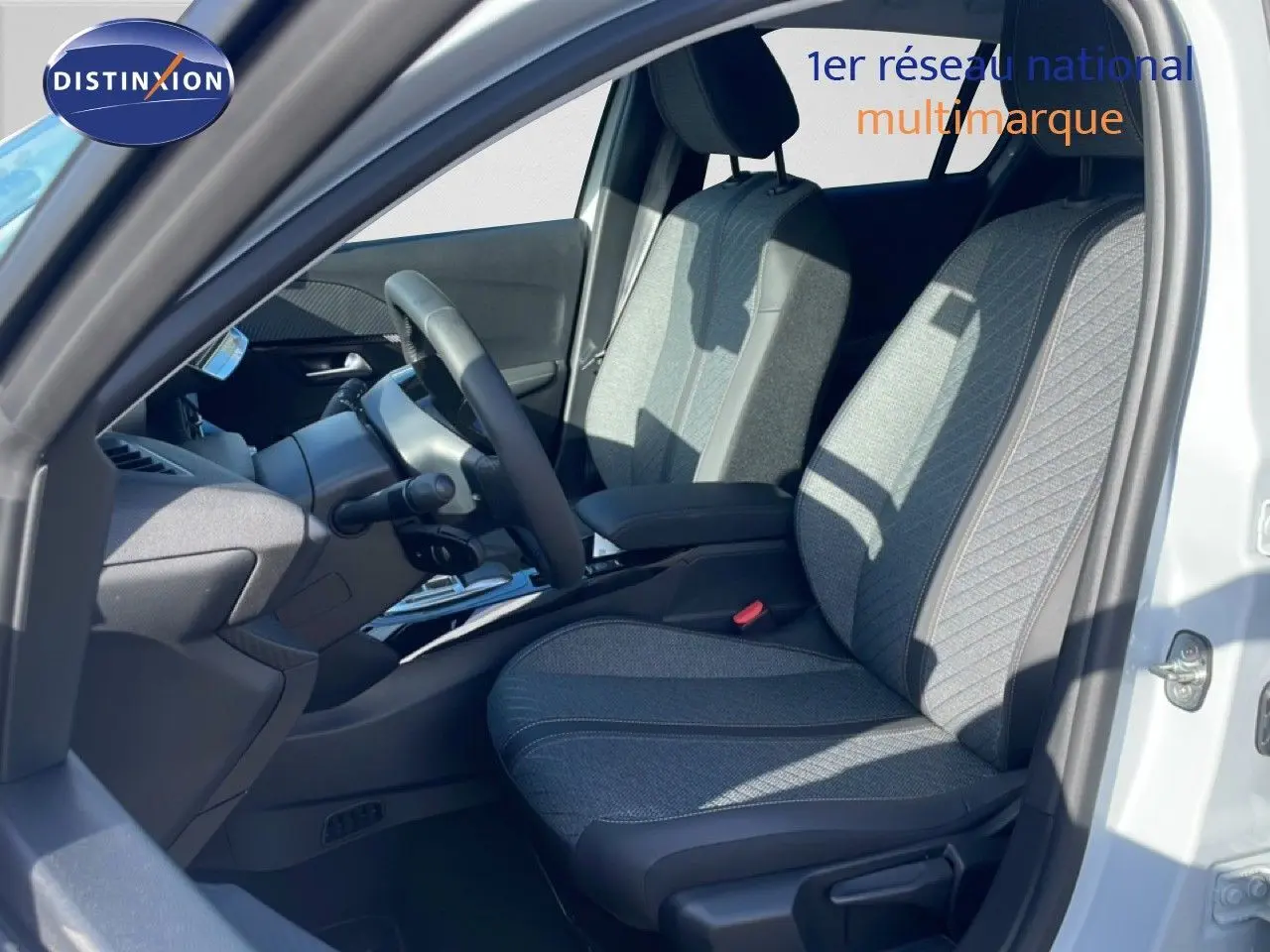 Vue intérieure côté conducteur d'une Peugeot 208 Hybrid blanche, sièges tissu gris avec détails noirs et volant multifonction.