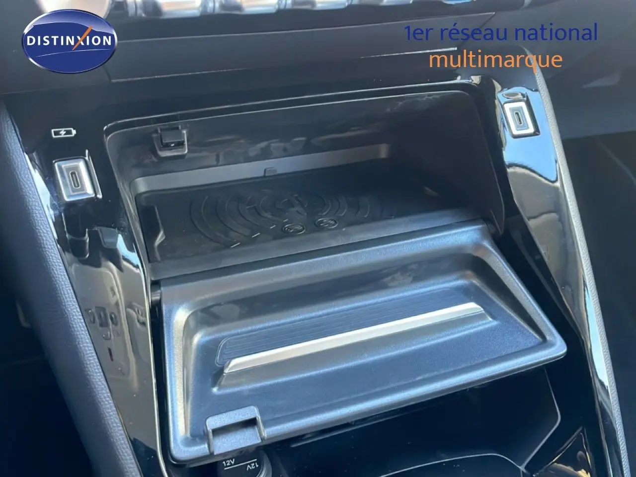 Gros plan sur la console centrale noire de la Peugeot 208 Hybrid 110ch, montrant un compartiment de rangement ouvert avec ports USB.