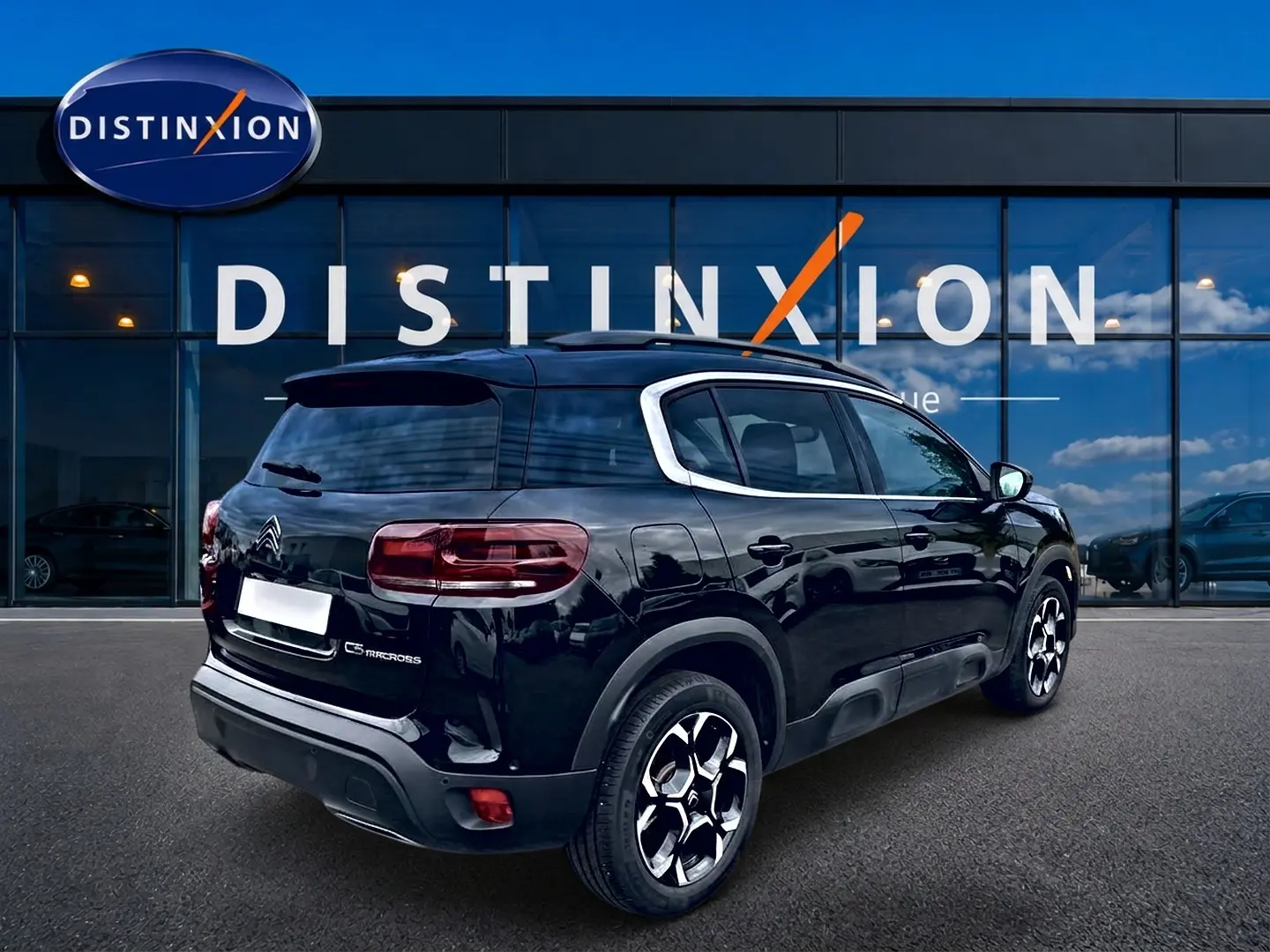 Vue 3/4 arrière droite d'un Citroën C5 Aircross noir avec jantes alu et barres de toit visibles devant un bâtiment.