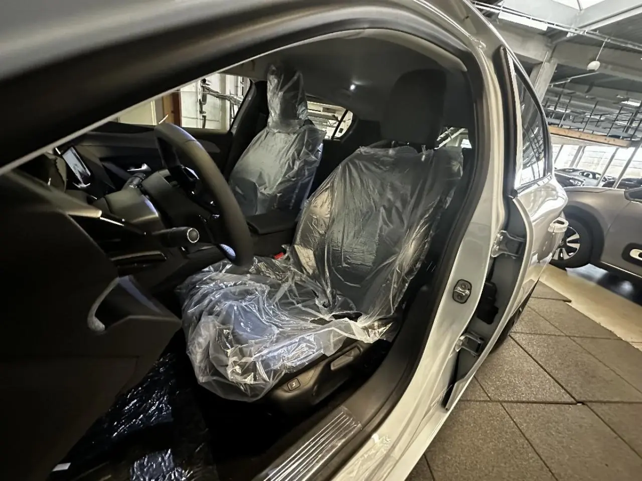 Vue intérieure côté conducteur de la Peugeot 308 blanc okenite 2024, sièges protégés par housses plastiques.