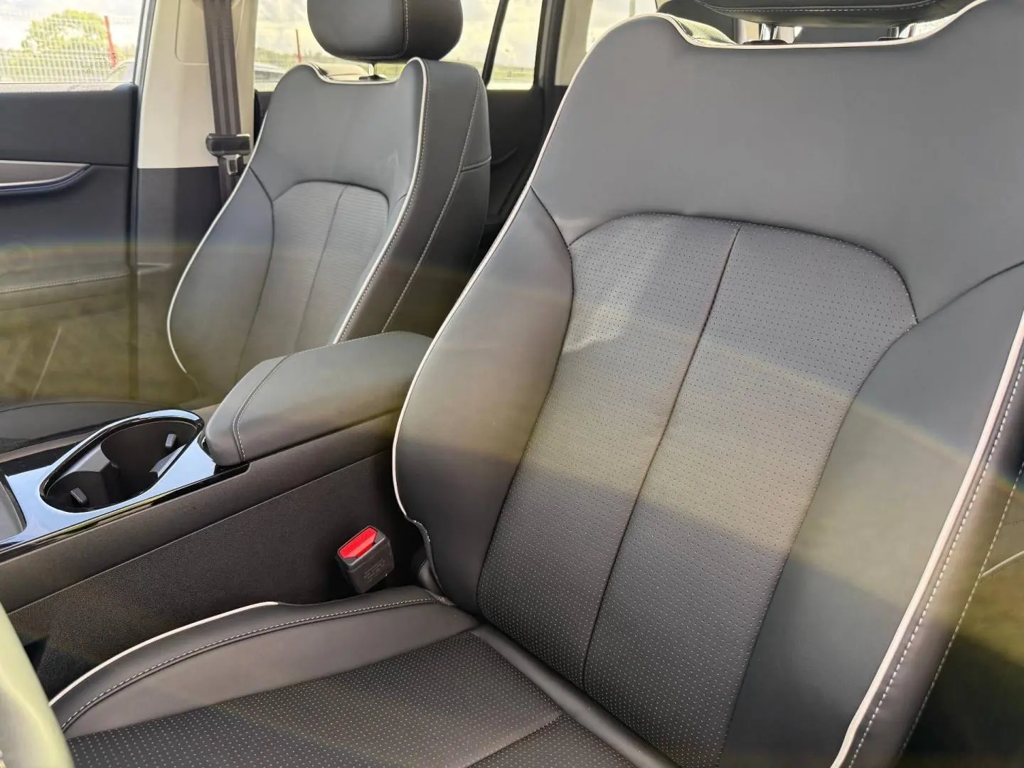 Gros plan sur les sièges avant en cuir synthétique noir avec surpiqûres blanches et accoudoir central dans un JAECOO J5 Phantom Grey.