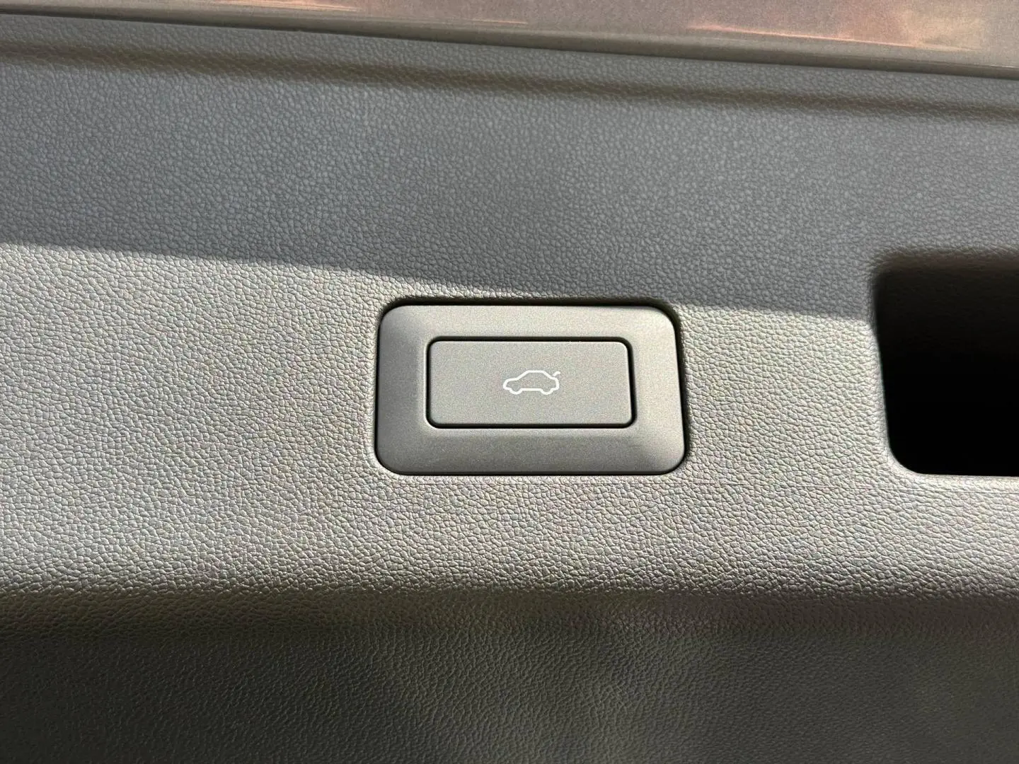 Bouton d'ouverture électrique du coffre sur panneau intérieur en plastique gris du JAECOO J5 Phantom Grey métal.
