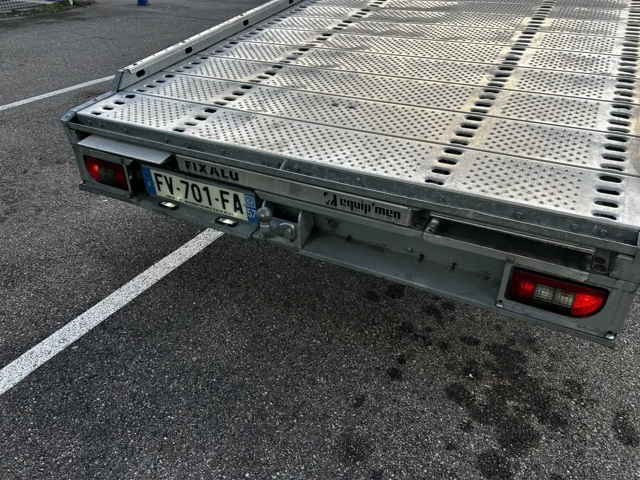 Plateau arrière en métal d'un Iveco Daily blanc, vu en gros plan depuis l'arrière droit avec plaque d'immatriculation française.