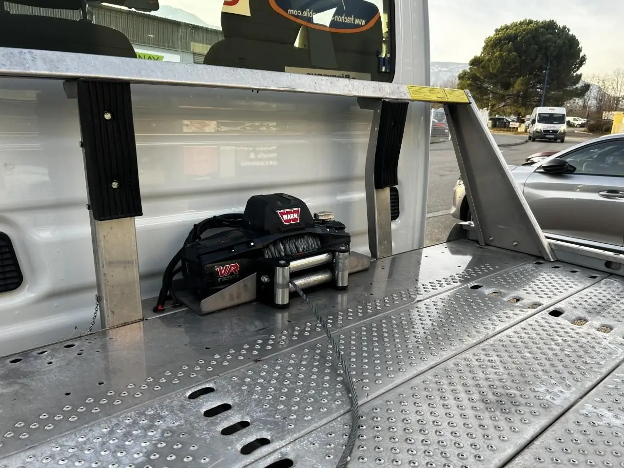 Gros plan sur le treuil Warn fixé à la benne arrière du plateau d’un Iveco Daily blanc, vue latérale droite.