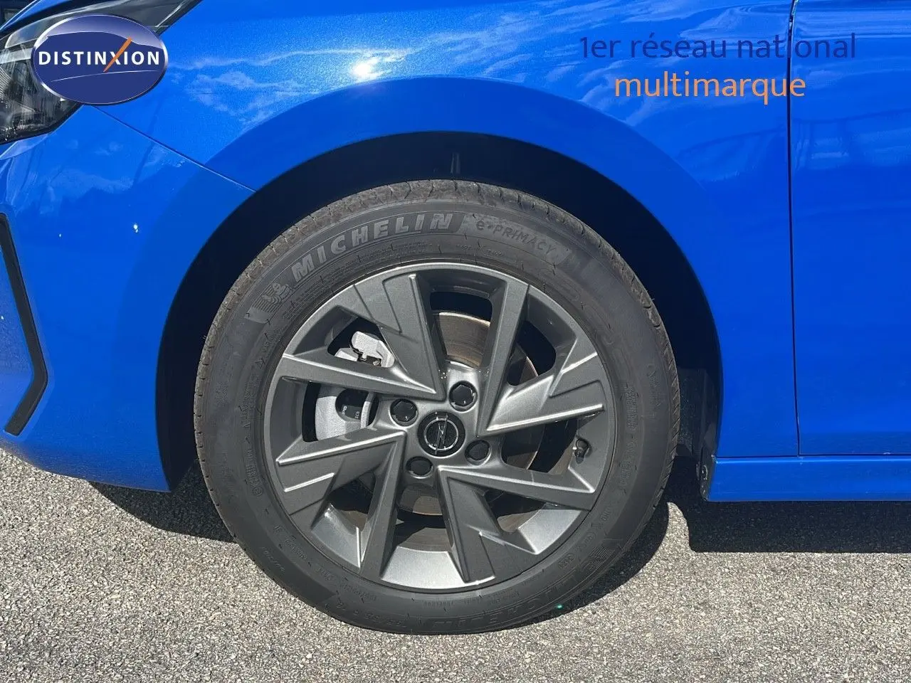Gros plan sur la roue avant gauche d'une Opel Corsa bleu voltaik métal avec jante alliage gris foncé.