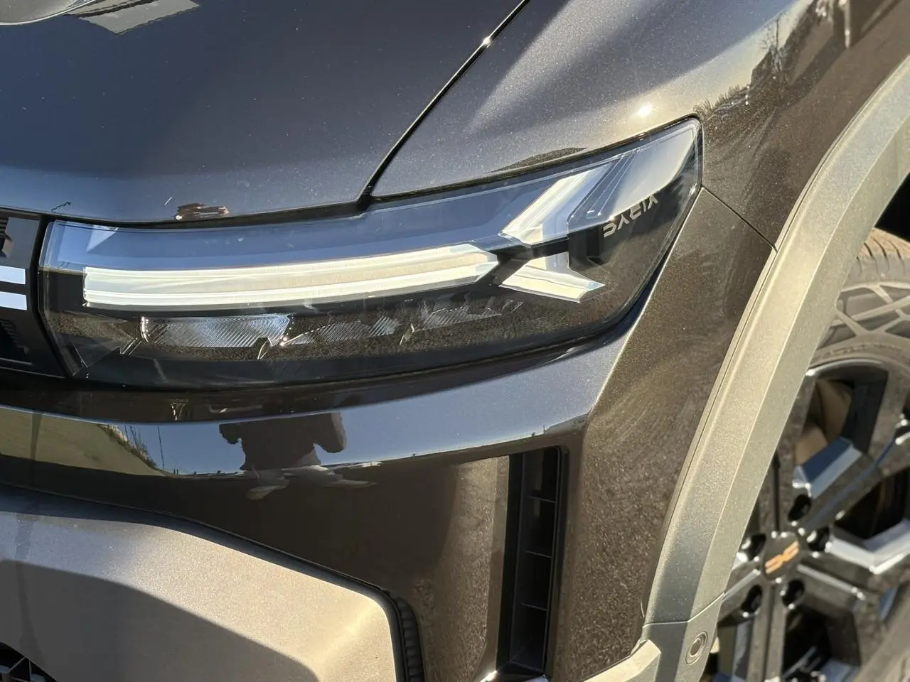 Gros plan sur le phare avant droit du Dacia Duster 2026 noir nacré avec jante alliage noire et détails modernes.
